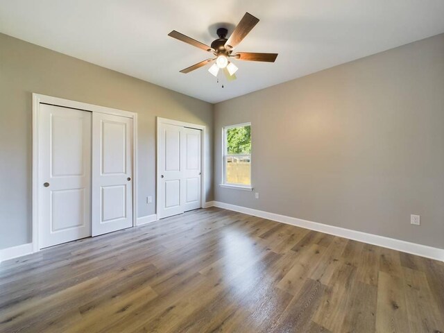 unfurnished bedroom featuring ceiling fan, multiple closets, and wood-type flooring