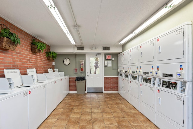 laundry room featuring stacked washer / dryer, washer and clothes dryer, and brick wall