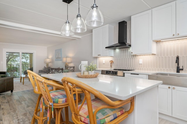 kitchen with pendant lighting, white cabinets, a kitchen bar, wall chimney range hood, and sink