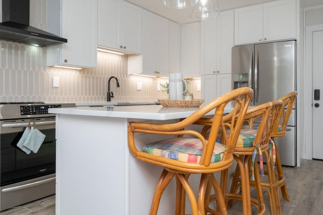 kitchen featuring light wood-type flooring, stainless steel appliances, wall chimney exhaust hood, and white cabinets