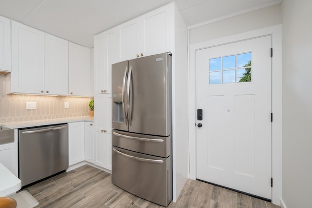 kitchen featuring backsplash, white cabinets, light hardwood / wood-style flooring, and stainless steel appliances