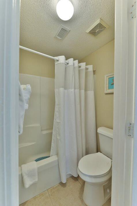 bathroom with tile patterned flooring, toilet, a textured ceiling, and walk in shower