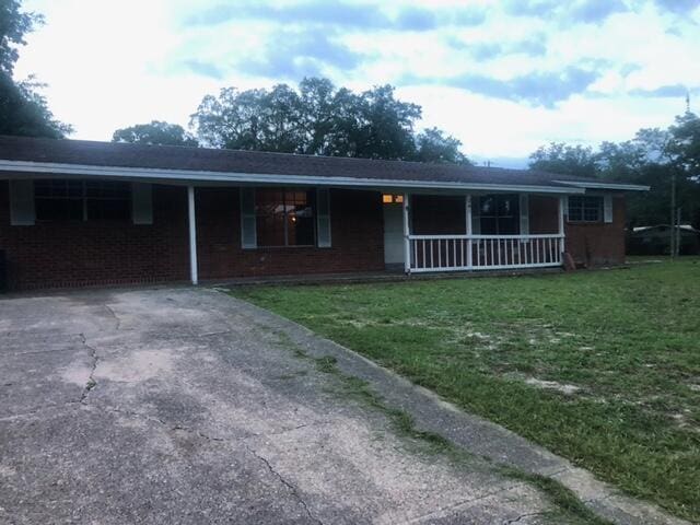 ranch-style home featuring brick siding, covered porch, a carport, driveway, and a front lawn