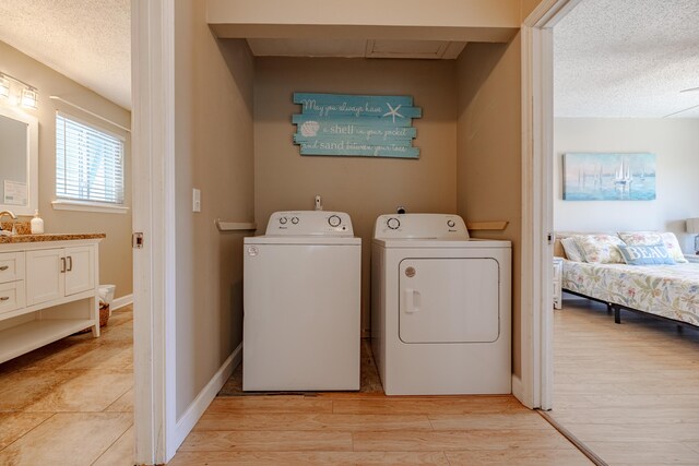 washroom with washing machine and clothes dryer, light hardwood / wood-style flooring, sink, and a textured ceiling