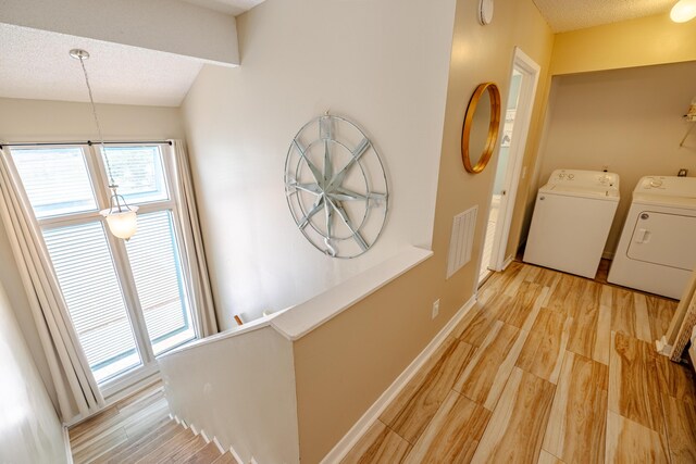 interior space featuring washing machine and clothes dryer, lofted ceiling, light wood-type flooring, and a textured ceiling