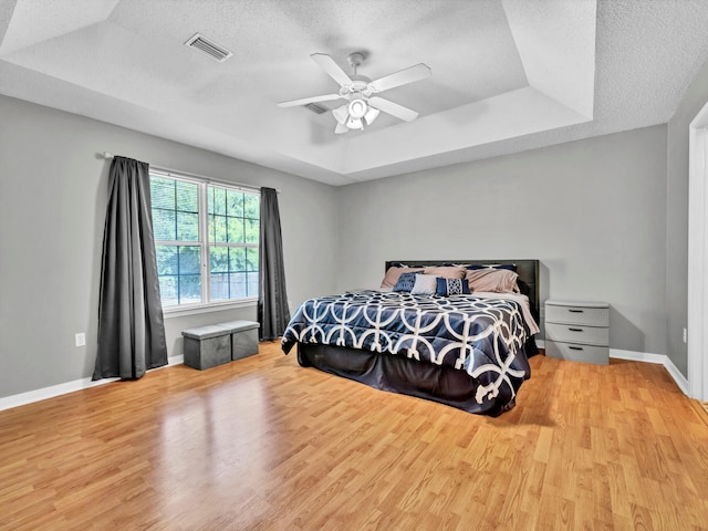 bedroom featuring a textured ceiling, ceiling fan, a raised ceiling, and light hardwood / wood-style floors