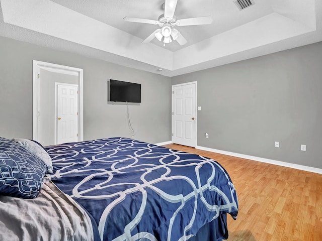 bedroom with ceiling fan, a tray ceiling, and wood-type flooring