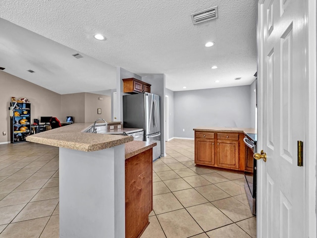 kitchen with light tile patterned flooring, sink, range with electric stovetop, stainless steel fridge, and a textured ceiling