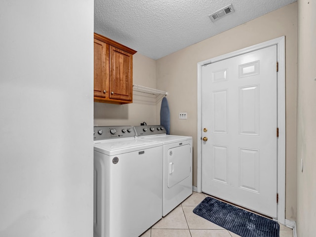 laundry room with light tile patterned flooring, independent washer and dryer, cabinets, and a textured ceiling