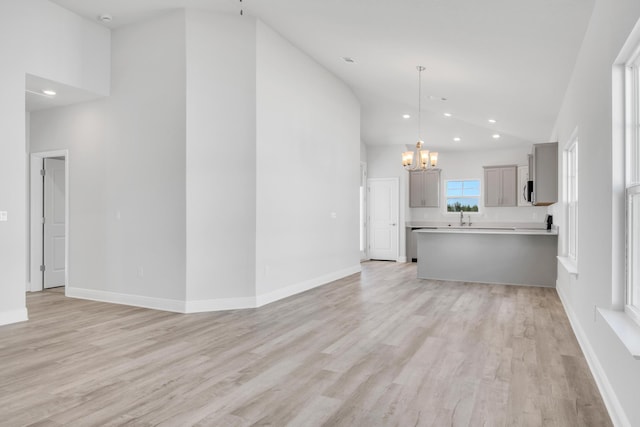 unfurnished living room with high vaulted ceiling, sink, light hardwood / wood-style flooring, and a notable chandelier