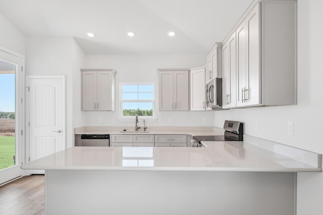 kitchen featuring sink, light hardwood / wood-style flooring, kitchen peninsula, stainless steel appliances, and white cabinets