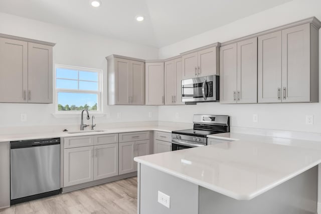 kitchen with gray cabinets, sink, kitchen peninsula, stainless steel appliances, and light wood-type flooring