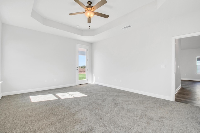 unfurnished room featuring ceiling fan, a tray ceiling, and dark carpet