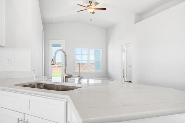 kitchen with lofted ceiling, sink, light stone counters, white cabinetry, and ceiling fan