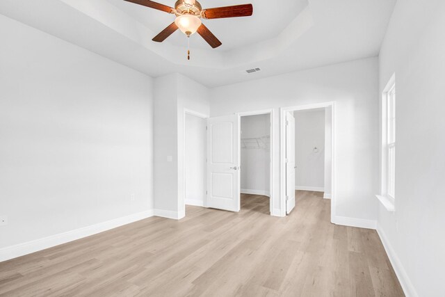 unfurnished bedroom featuring ceiling fan, a raised ceiling, light wood-type flooring, and a walk in closet