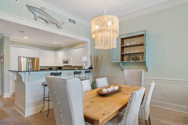 dining space with light hardwood / wood-style floors, a chandelier, and ornamental molding
