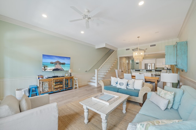 living room with ornamental molding, ceiling fan with notable chandelier, and light hardwood / wood-style floors