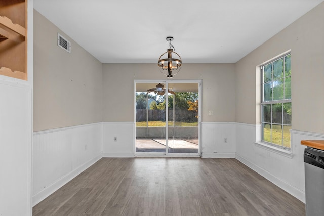 unfurnished dining area featuring plenty of natural light, visible vents, wood finished floors, and wainscoting