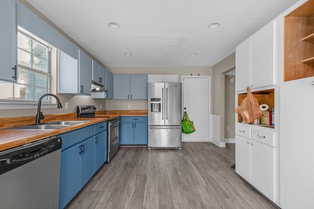 kitchen with under cabinet range hood, blue cabinets, stainless steel appliances, a sink, and wooden counters