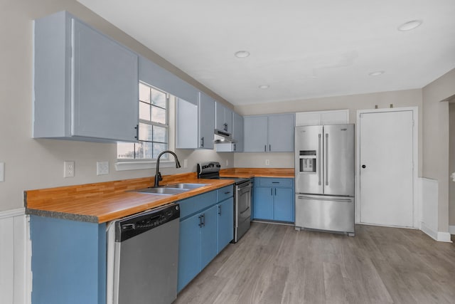 kitchen with blue cabinetry, stainless steel appliances, sink, butcher block counters, and light wood-type flooring