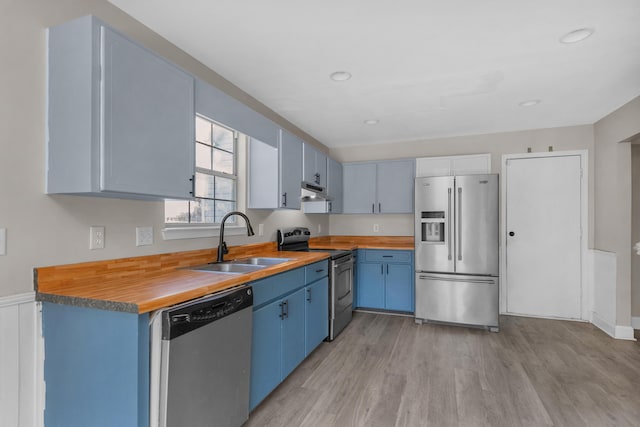 kitchen featuring light wood finished floors, wood counters, appliances with stainless steel finishes, blue cabinets, and a sink