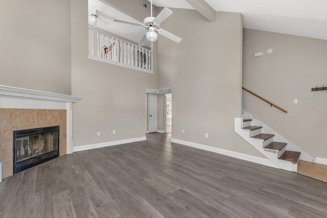 unfurnished living room with ceiling fan, wood finished floors, baseboards, stairs, and a tiled fireplace