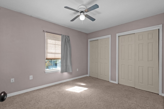 unfurnished bedroom with multiple closets, carpet flooring, baseboards, and a ceiling fan