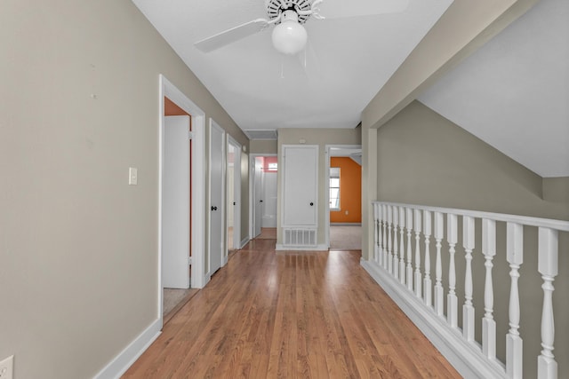 hall featuring light wood-style flooring, visible vents, vaulted ceiling, and baseboards