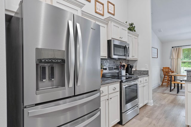 kitchen with lofted ceiling, stainless steel appliances, tasteful backsplash, dark stone counters, and light hardwood / wood-style flooring