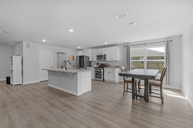 kitchen featuring appliances with stainless steel finishes, a center island with sink, sink, light wood-type flooring, and white cabinetry