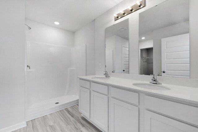 bathroom with hardwood / wood-style flooring, a shower, and dual bowl vanity