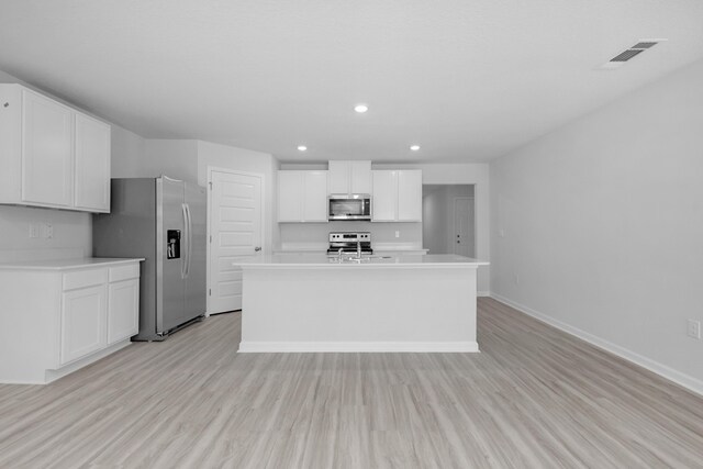 kitchen featuring white cabinets, stainless steel appliances, a center island with sink, and light wood-type flooring