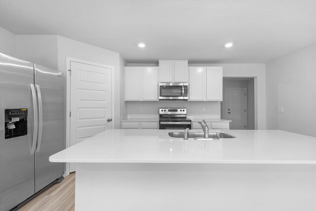 kitchen with sink, a center island with sink, light wood-type flooring, and stainless steel appliances