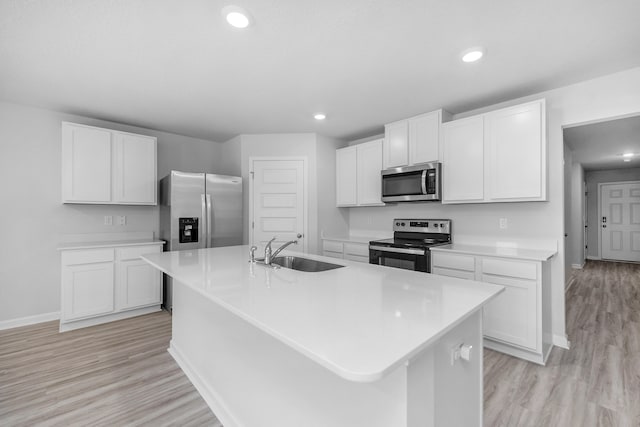 kitchen with white cabinets, light hardwood / wood-style floors, appliances with stainless steel finishes, sink, and a center island with sink