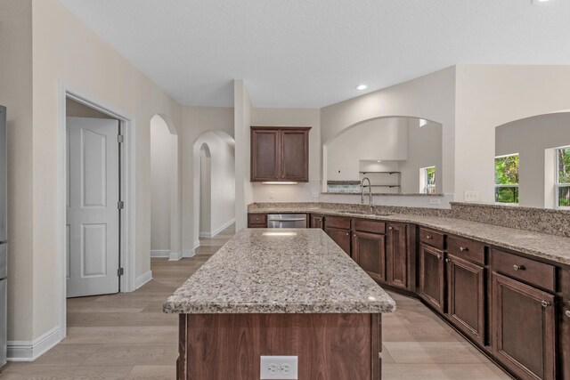 kitchen with a kitchen island, sink, light wood-type flooring, and light stone countertops