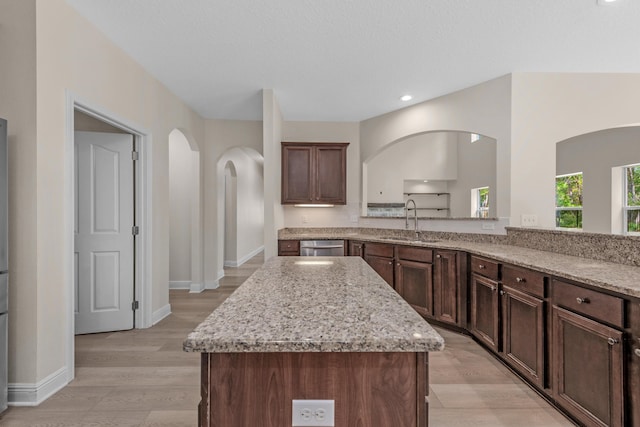 kitchen featuring a sink, light stone counters, a kitchen island, and dark brown cabinetry