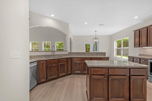 kitchen with appliances with stainless steel finishes, sink, light wood-type flooring, and light stone countertops