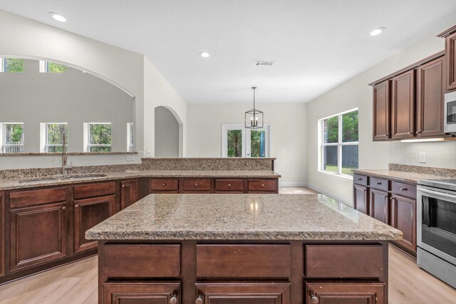 kitchen with sink, stainless steel electric range, a healthy amount of sunlight, and light stone counters