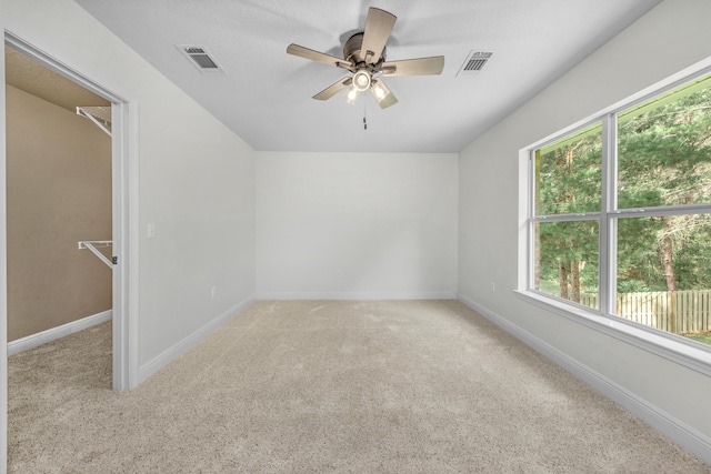 empty room featuring a ceiling fan, visible vents, light carpet, and baseboards