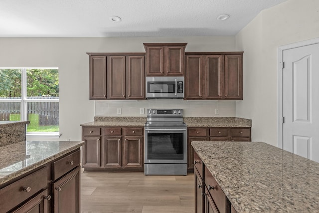 kitchen with light stone counters, stainless steel appliances, backsplash, dark brown cabinets, and light wood-type flooring