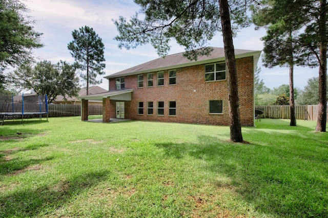 back of house featuring a trampoline, a fenced backyard, a lawn, and brick siding