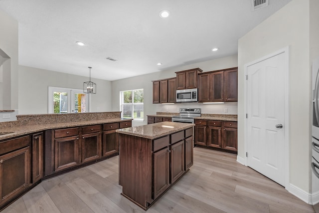 kitchen with stainless steel appliances, pendant lighting, dark brown cabinetry, light wood-type flooring, and stone countertops