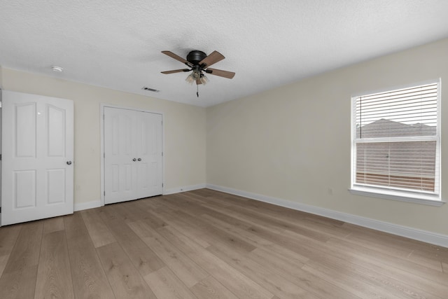 unfurnished bedroom featuring a textured ceiling, light wood-type flooring, visible vents, and baseboards