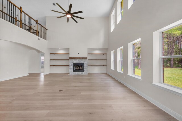 unfurnished living room with a stone fireplace, light wood-type flooring, and a healthy amount of sunlight