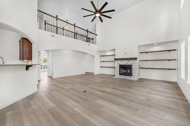 unfurnished living room featuring light wood-style flooring, a fireplace, visible vents, a ceiling fan, and baseboards