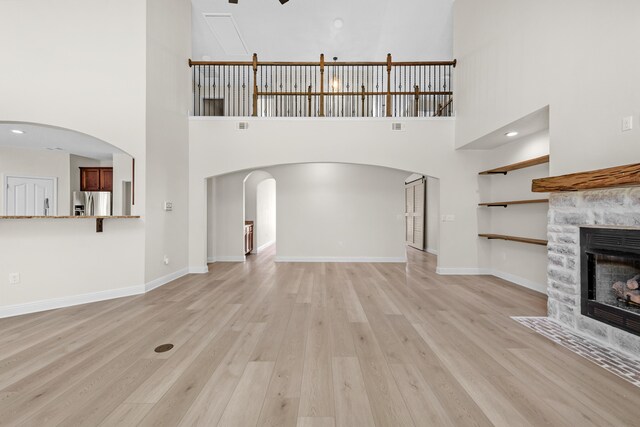 unfurnished living room with a fireplace, light hardwood / wood-style flooring, and a high ceiling