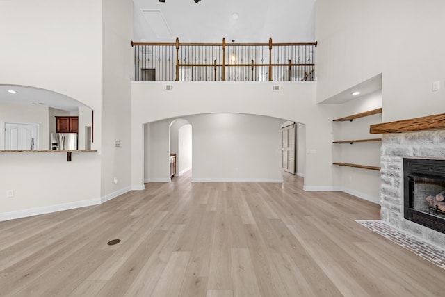 unfurnished living room featuring arched walkways, a tiled fireplace, baseboards, and light wood-style floors