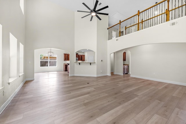 unfurnished living room featuring arched walkways, light wood finished floors, visible vents, baseboards, and ceiling fan with notable chandelier