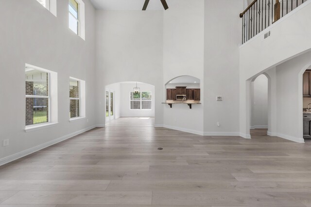 unfurnished living room with light hardwood / wood-style flooring, a wealth of natural light, and a high ceiling