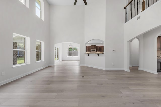 unfurnished living room featuring light wood-type flooring, arched walkways, visible vents, and baseboards